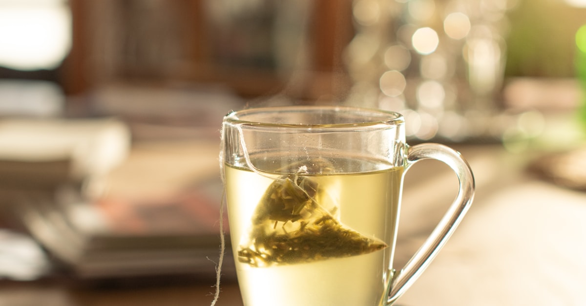Dampfende Tasse Kräutertee auf alten Büchern als ruhige Geste der Selbstfürsorge bei Liebeskummer